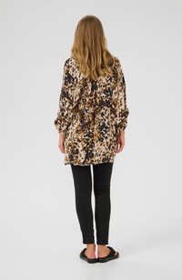 Leopard print blouse in beige, brown, and black, featuring long sleeves and a relaxed fit, paired with black leggings and flat sandals.