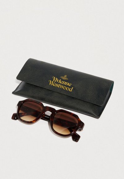 Gafas de sol de carey con lentes marrones degradados, que presentan un marco rectangular grueso. Acompañadas de un estuche de cuero verde con un logo dorado.