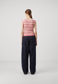 Haut en tricot rayé rose et blanc avec des manches courtes, associé à un jean en denim bleu foncé ample avec deux poches arrière et des coutures visibles.
