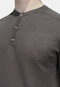 Maglietta henley grigio scuro realizzata in un tessuto morbido, con scollatura rotonda, pattina a tre bottoni e una sottile texture a costine sul collo.
