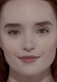 Close-up van een gezicht met lichte huid, rood haar en bruine ogen; gladde textuur, minimale make-up en een neutrale lipkleur.