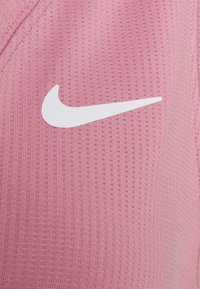 Roze sporttop van gestructureerde stof, met een wit Nike-swooshlogo. Het ontwerp heeft ribbels over het hele kledingstuk.