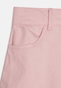 Ljust rosa denimtyg med en synlig ficka och sömnadsdetaljer. Texturen är slät med en lätt töjbarhet.