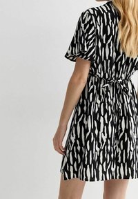 Černé a bílé krátké šaty s krátkými rukávy, které mají texturovaný vzor vertikálních pruhů a vázání vzadu v pase.