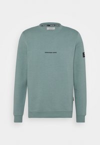 Groene sweatshirt van zacht materiaal, met een ronde hals, lange mouwen en een logo "REDEFINED REBEL" op de borst gedrukt.