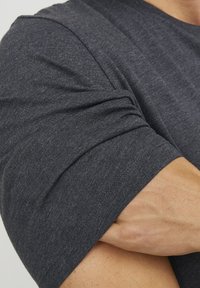 Mørkegrå kortærmet t-shirt i et blødt, tekstureret stof. Har opprullede ærmer og en tætsiddende pasform, der fremhæver en muskuløs arm.