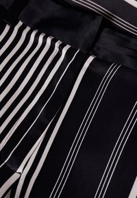 Black fabric with white vertical stripes, featuring a smooth texture and sleek design. Accentuated edges and a tailored waistband.