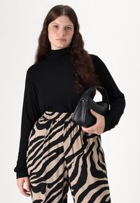 Svart langermet topp kombinert med beige bukser med svart zebra-striper og en liten svart skulderveske med buet håndtak.