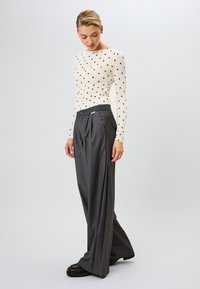 Lange mouwen, crème top met zwarte stippen, gecombineerd met hoge taille, wijde grijze broek. Zwarte chunky schoenen maken de outfit compleet.