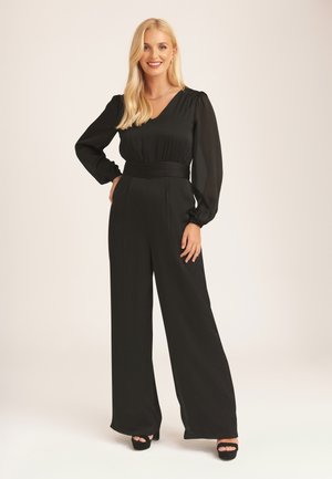 Black jumpsuit with long sleeves, v-neck, and belted waist. The fabric has a smooth texture and wide-leg pants. Black open-toe heels.