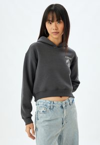Sudadera gris cortada de tela suave con un gráfico en la parte frontal y puños acanalados, combinada con jeans acolchados de color azul claro.