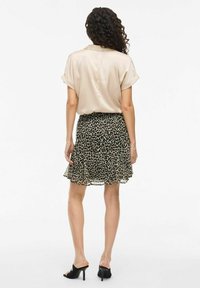 Blouse en satin beige clair avec des manches courtes retroussées, associée à une jupe à volants noire à imprimé léopard. Des talons ouverts noirs viennent compléter le look.