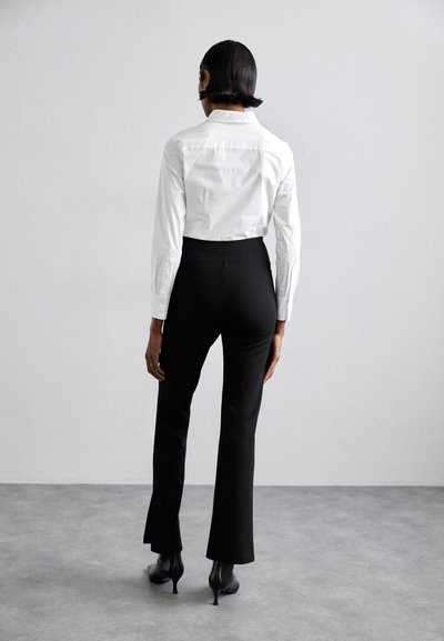 White button-up shirt with long sleeves paired with high-waisted black flared trousers and black pointed heels, viewed from the back.