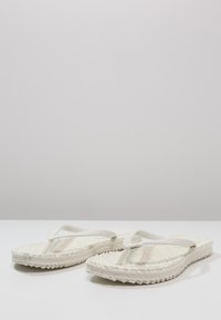 Witte slippers met geweven stro zolen, vlakke rubberen bandjes en een getextureerde voetbed. Eenvoudig ontwerp met een neutraal kleurenpalet.