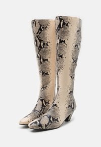 Bottes beige mi-hauteur avec motif en cuir de serpent noir, bouts pointus et talons bas inclinés, posées côte à côte sur fond blanc.