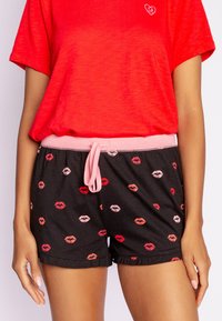 Röd kortärmad skjorta med hjärtformad design, kombinerad med svarta shorts med flerfärgade läpptryck och en rosa dragsko i midjan.