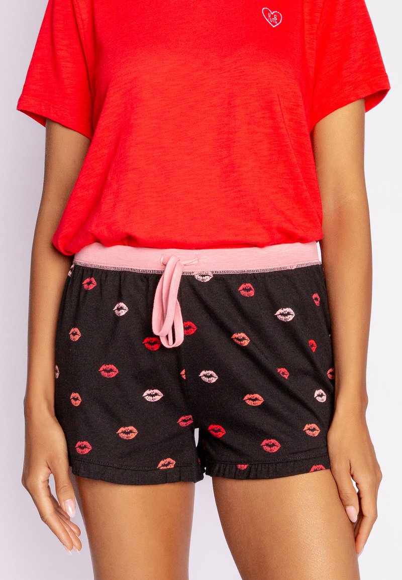 Rode t-shirt met korte mouwen en hartontwerp, gecombineerd met zwarte shorts met multicolored lippenprints en een roze trekkoord in de taille.