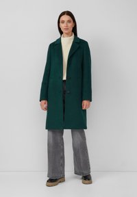 Groene, wolblend lange jas met revers, drie knopen en zijzakken, gecombineerd met een crèmekleurige trui en grijze flared jeans.