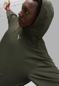 Olivgrüner Kapuzenpullover aus weichem Stoff, mit einer Kängurutasche und einem weißen Puma-Logo auf der Brust, ausgestattet mit verstellbaren Kordeln.