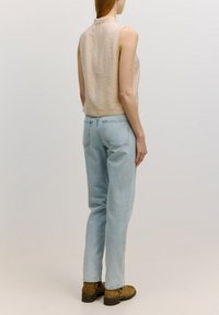 Beige ärmelloses Oberteil mit hohem Kragen, kombiniert mit hellblauen Jeans im lässigen Schnitt und braunen Ankle Boots.