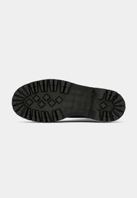 Semelle de botte noire avec des sculptures profondes et des motifs de grip en forme de losange sur un fond clair uni.