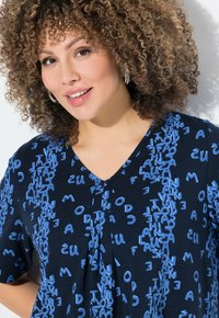 Námořnický top s krátkým rukávem, zdobený náhodným textovým vzorem v světle modré barvě. V-podprsenkový design, lehká tkanina s mírně strukturovaným povrchem.