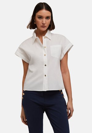 Witte shirt met korte mouwen, knoopsluiting aan de voorkant, een enkel zakje op de linkerborst en sluiting met goudkleurige knopen. Gladde katoenen stof.