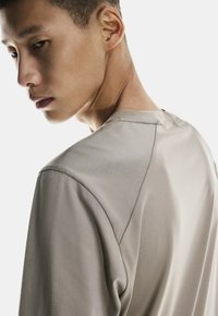 Ljust grå långärmad skjorta med rund halsringning, strukturerad tyg och unik axelsömnadsdesign. Har en smidig, minimalistisk stil.