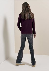 Haut à manches longues de couleur violet foncé associé à un jean en denim gris. La tenue présente un design simple, une coupe droite, et est complétée par des baskets beiges.