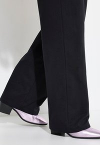 Zwarte wijde broek en glanzende, lichtpaarse puntige schoenen met lage hakken. Glad van textuur en gestroomlijnd ontwerp zichtbaar.