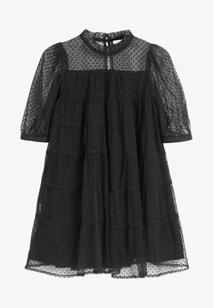 Czarna sukienka w groszki z przezroczystej tkaniny, z wysokim kołnierzem, krótkimi bufkami i wielowarstwowym krojem. Teksturowana i warstwowa dla zwiększenia objętości.
