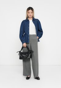 Denims krekls ar pogām, balts tops, pelēki šķērsgriezuma bikses; tur melnu teksturētu rokassomu ar mezglotiem rokturiem; ikdienišķi apavji.