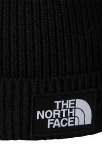 Svart strikket lue med vertikale ribber, med en rektangulær svart etikett med "THE NORTH FACE"-logo i hvitt, plassert foran.