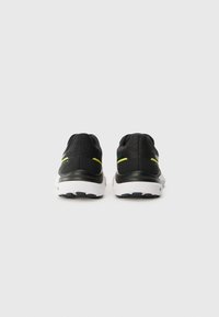 Chaussures de sport noires avec une tige texturée, mettant en avant des accents jaunes, une semelle intermédiaire blanche et une semelle extérieure en caoutchouc avec un motif de crantage.