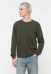 Chemise à manches longues, verte olive, avec un col rond et une poche poitrine, fabriquée en tissu doux, dotée de poignets côtelés et d'une coupe décontractée.