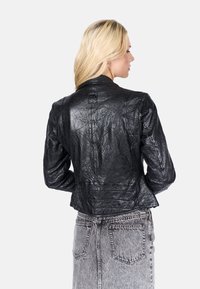 Chaqueta de cuero negra con un acabado texturizado, que presenta un corte ajustado, cuello y costuras visibles. Llevada sobre una falda de mezclilla gris.