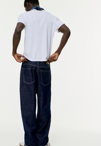 Witte T-shirt met korte mouwen, gecombineerd met donkerblauwe spijkerbroek. Het shirt heeft een ronde hals en de jeans hebben twee achterzakken.