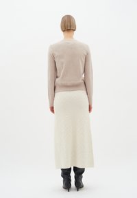 Helles beige Strickoberteil und cremefarbener Maxirock mit Zickzackmuster, kombiniert mit schwarzen spitzen Stiefeletten. Glatte Texturen, figurbetonter Schnitt.