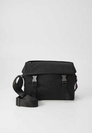 Sac messager noir en nylon avec fermoir à rabat, bandoulière ajustable et quincaillerie en métal. Présente un logo embossé à l'avant.