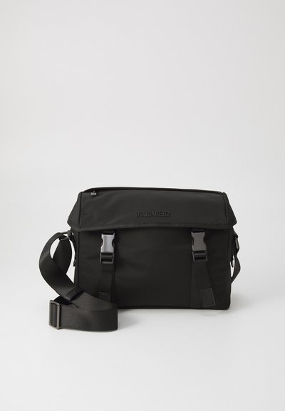 Sac messager noir en nylon avec fermoir à rabat, bandoulière ajustable et quincaillerie en métal. Présente un logo embossé à l'avant.
