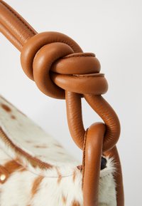 Mango marrón enredado como asa unido a un bolso texturizado color crema con manchas marrones. El material contrasta entre el cuero suave y la piel suave.