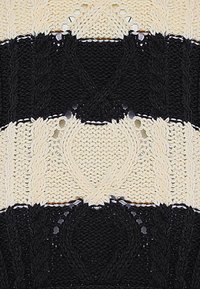 Kötött textil, amely felváltva fekete és krém színű szakaszokat tartalmaz, texturált kábel mintákkal és fényes részletekkel, amely ellentétes dizájnt alkot.