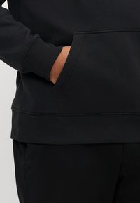 Hanorac negru cu buzunar marsupiu, manșete și tiv striate. Confecționat dintr-un material moale, cu o textură netedă.