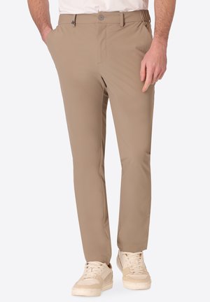 Uomo con pantaloni beige slim fit con tasche laterali e sneakers bianche casual con lacci su sfondo neutro.