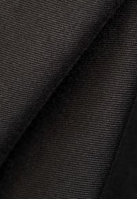 Primer plano de tela negra acanalada doblada que muestra un tejido texturizado diagonal y detalles de material suave.