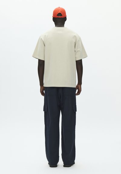 Γκρι ανοιχτόχρωμο oversized t-shirt με κοντά μανίκια, συνδυασμένο με μπλε ναυτικό cargo παντελόνια με πλαϊνές τσέπες. Το σύνολο ολοκληρώνεται με κόκκινο καπέλο.