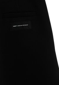 Pantalones negros con una textura suave, que presentan un bolsillo cosido y una etiqueta tejida que dice "MWM mod wave movement."