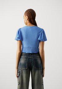 Blå teksturert crop top med korte puffermer og smocket liv, kombinert med m�ørk denim brede bukser med lapperlommer.