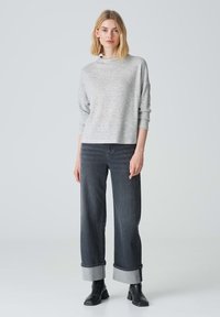 Helle, graue Textur-Strickjacke mit hohem Kragen, kombiniert mit dunkelgrauen, weiten Jeans mit umgeschlagenem Saum und schwarzen, knöchelhohen Stiefeln.