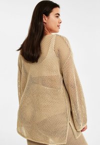 Beige, oversized trui van opengebreide stof, met lange mouwen en zijsplitten voor een ontspannen pasvorm. Geweven mesh ontwerp.